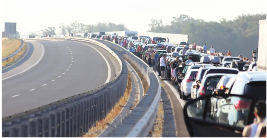 Stationary traffic filling the lanes of a highway, with drivers standing outside their cars, while the opposite carriageway runs empty.